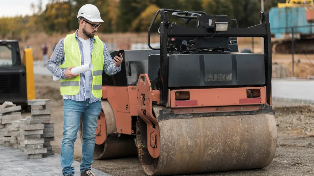 Un homme se tient à côté d'un rouleau sur un chantier de construction pour le nivellement de terrain.