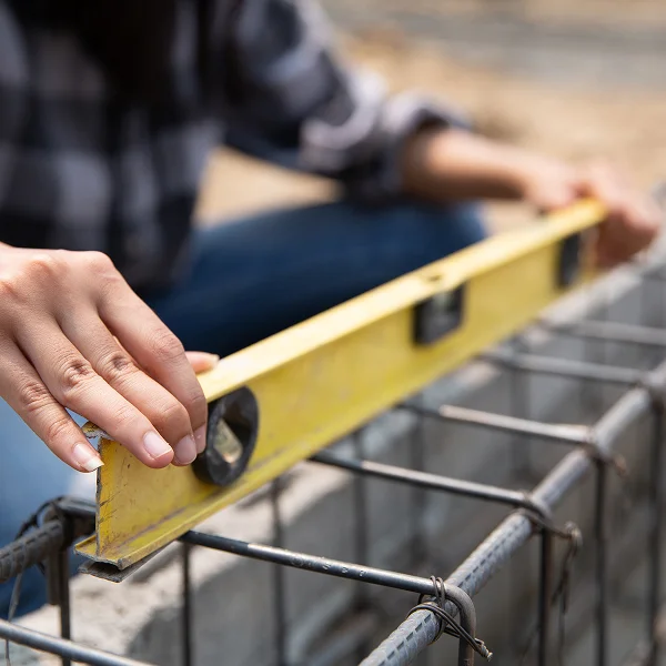 Une personne tient un niveau contre un mur en béton, illustrant l'installation d'un drain français.